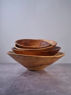 Set of three wooden bowls stacked on a gray surface with a gray background