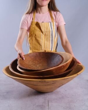 Person holding three wooden bowls with a plain background