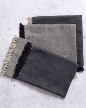 Four cloth dinner napkins double sided in black and gray with frayed edges on a light gray background