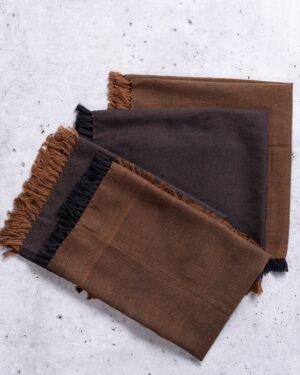 Four brown and black double sided cloth napkins with frayed edges on a textured white surface