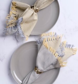 Gray plates with folded napkins featuring fringe details on a light gray background